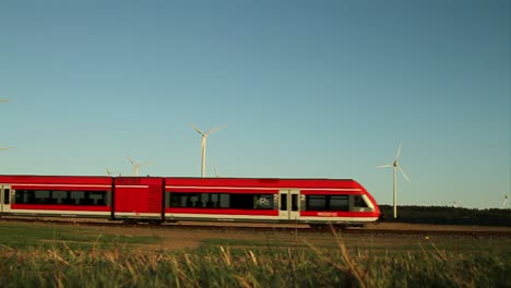 red train crossing rural landscape with wind turbines against a clear blue sky, daytime