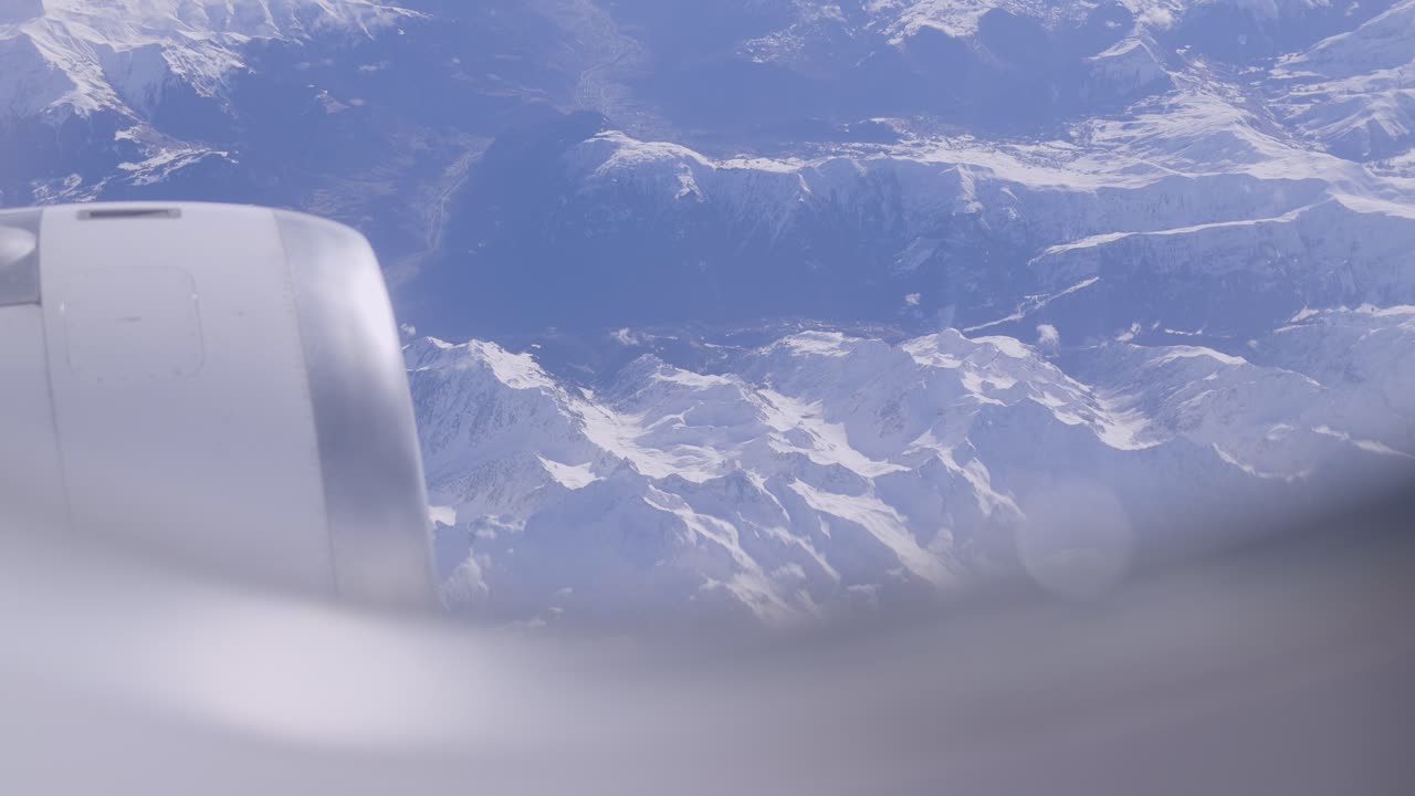 View of snow-capped mountains from airplane window, showing engine and clear sky