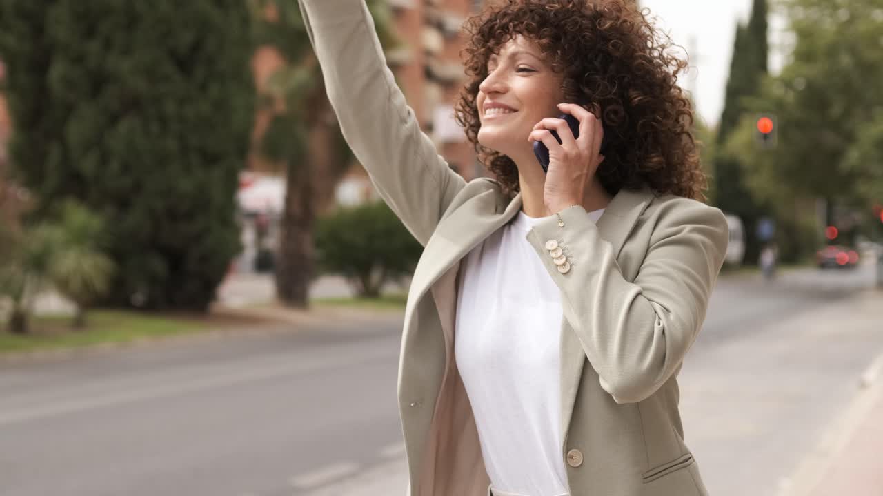 Happy businesswoman signaling taxi and using cellphone near street