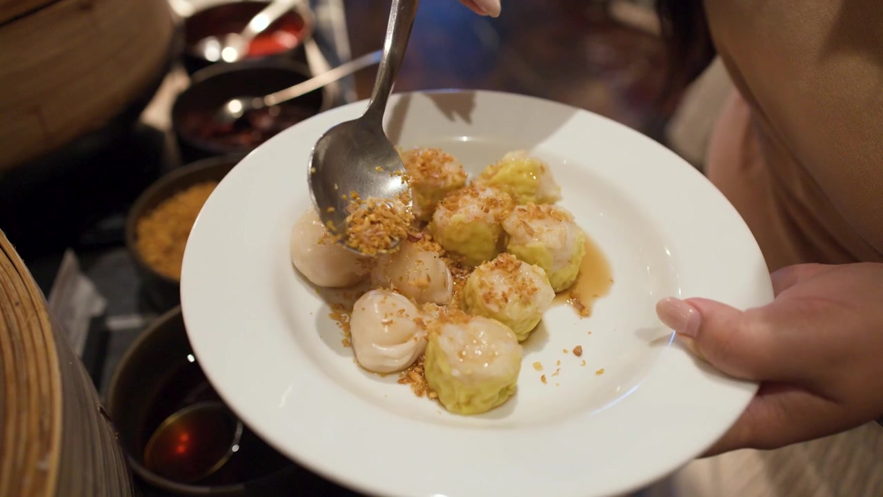 Primo piano di una mano che aggiunge aglio fritto a dei dim sum su un piatto bianco.