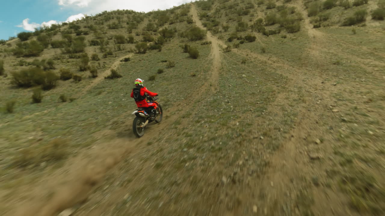 Person in red rides motorbike along bushy hills fpv. Fearless racer in helmet drives vehicle to mountain peak at motocross racing. Extreme sport at highland