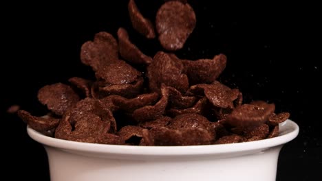 chocolate cereal pieces cascade into a white bowl against a black backdrop, creating a dynamic and appetizing visual