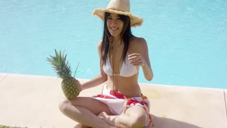 Una-Mujer-Con-Piña-Y-Sombrero-De-Paja-Se-Sienta-Junto-A-La-Piscina