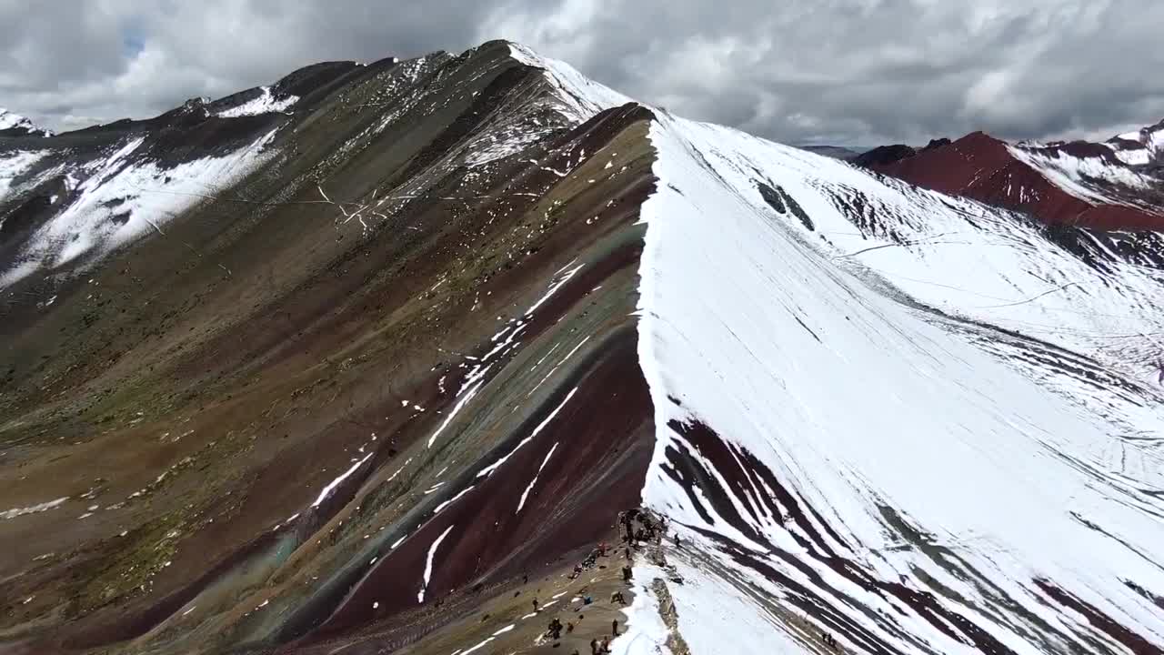 vista de avión no tripulado en perú volando sobre la montaña arco iris en cuzco, mostrando a la gente mirando fijamente la cordillera mitad nevada mitad coloreada