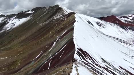 drone view in peru flying over rainbow mountain in cuzco, showing people staring at the half snowed half colored range