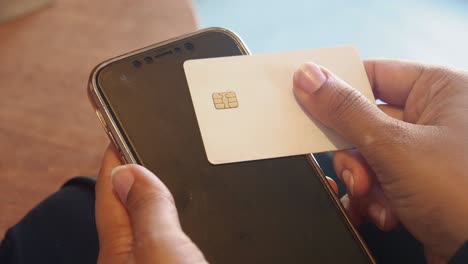 closeup of a hand holding a credit card and a smartphone, likely for making a contactless payment.