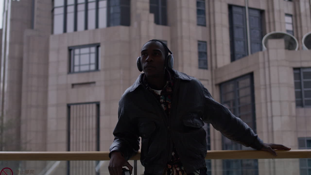 Fotografo artista freelance afroamericano che si guarda intorno nel paesaggio urbano metropolitano mentre ascolta musica, indossando cuffie alla moda.