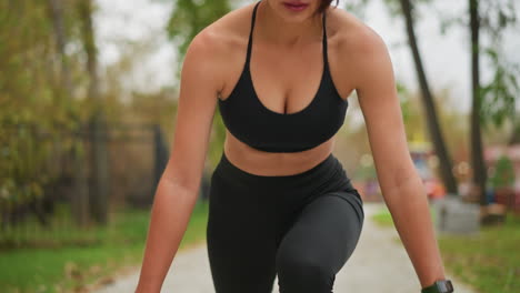 close-up of girl stretching leg out and squatting down with hands on ground, preparing to run in athletic outdoor environment. focus on movement, fitness, and athletic posture for active lifestyle