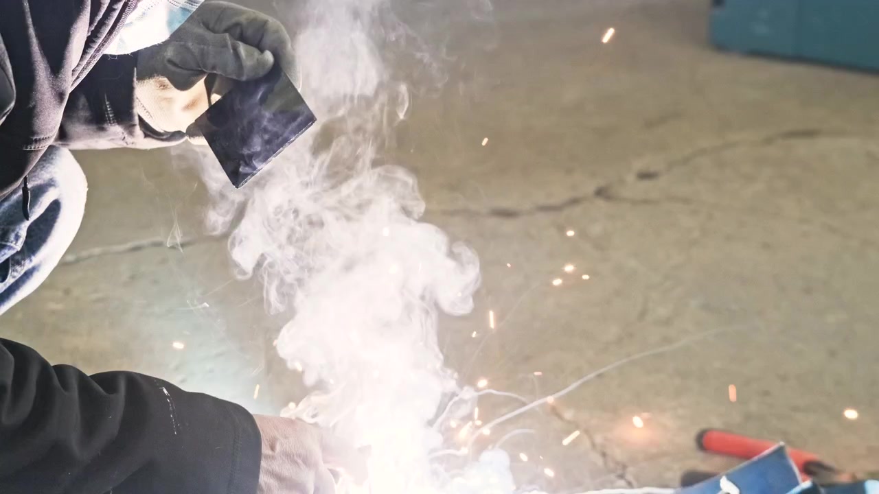 Welder With Medical Mask Welding Metal In A Factory With A Tinted Welding Glass For Eye Protection From Sparks - close up, slow motion