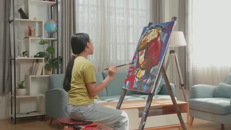 side view of an asian artist girl holding paintbrush mixed colour and thinking before painting a girl's hair on the canvas
