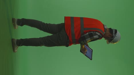 full body back view of asian male engineer with safety helmet using a tablet drawing the wind turbine blueprint while standing in the green screen background studio, during sunset or sunrise time
