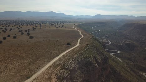 Aerial-view-of-a-badlands-desert-area-with-a-dirt-road-and-mountains-on-the-horizon