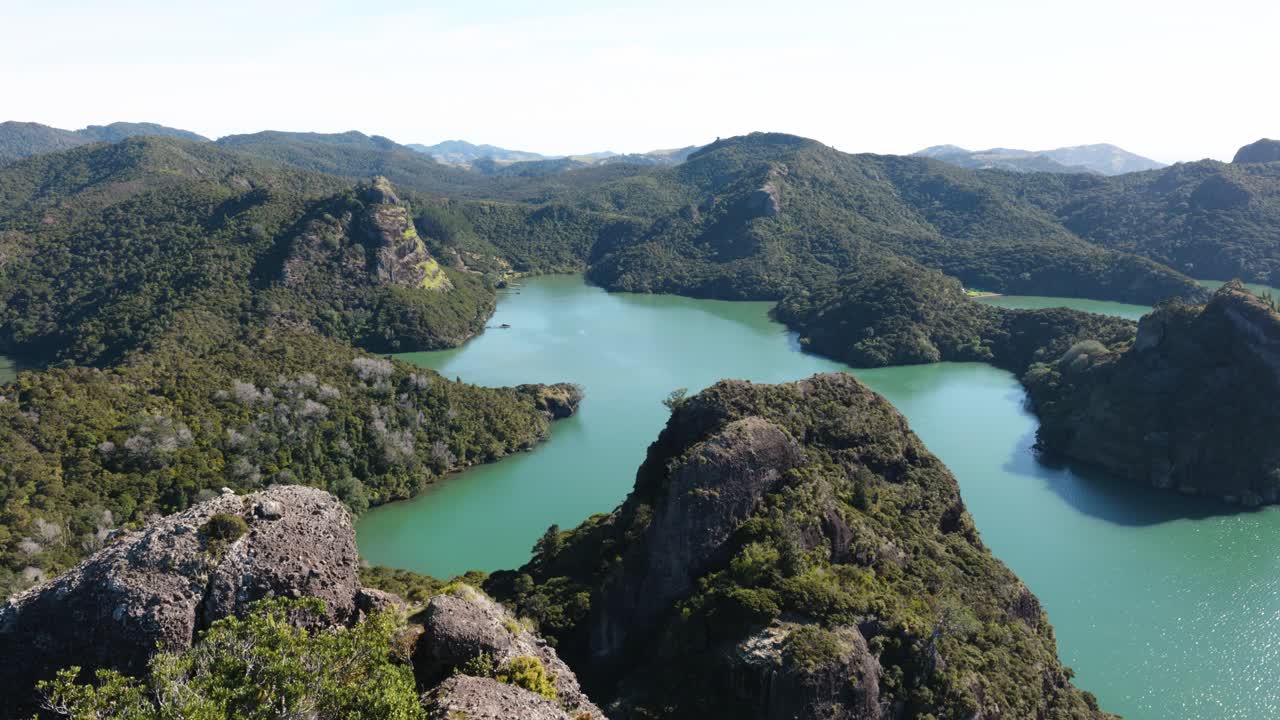 View of a bay with mountains, greenery and turquoise water on a sunny day in Duke's Nose, Northland, New Zealand.