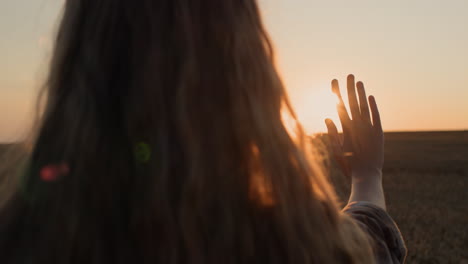 a girl with beautiful long hair holds out her hand to the setting sun.