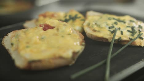 Close-up-of-vegan-french-toast-presented-on-a-black-cutting-board-while-chef-puts-fresh-chives-on-the-toast