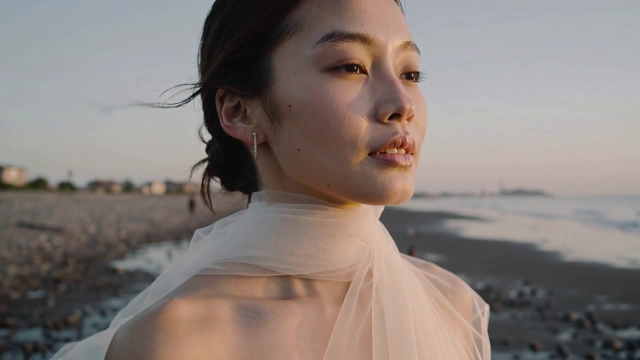 Reacting to breeze lifting sheer scarf, adult woman opening eyes and gazing toward horizon at coast