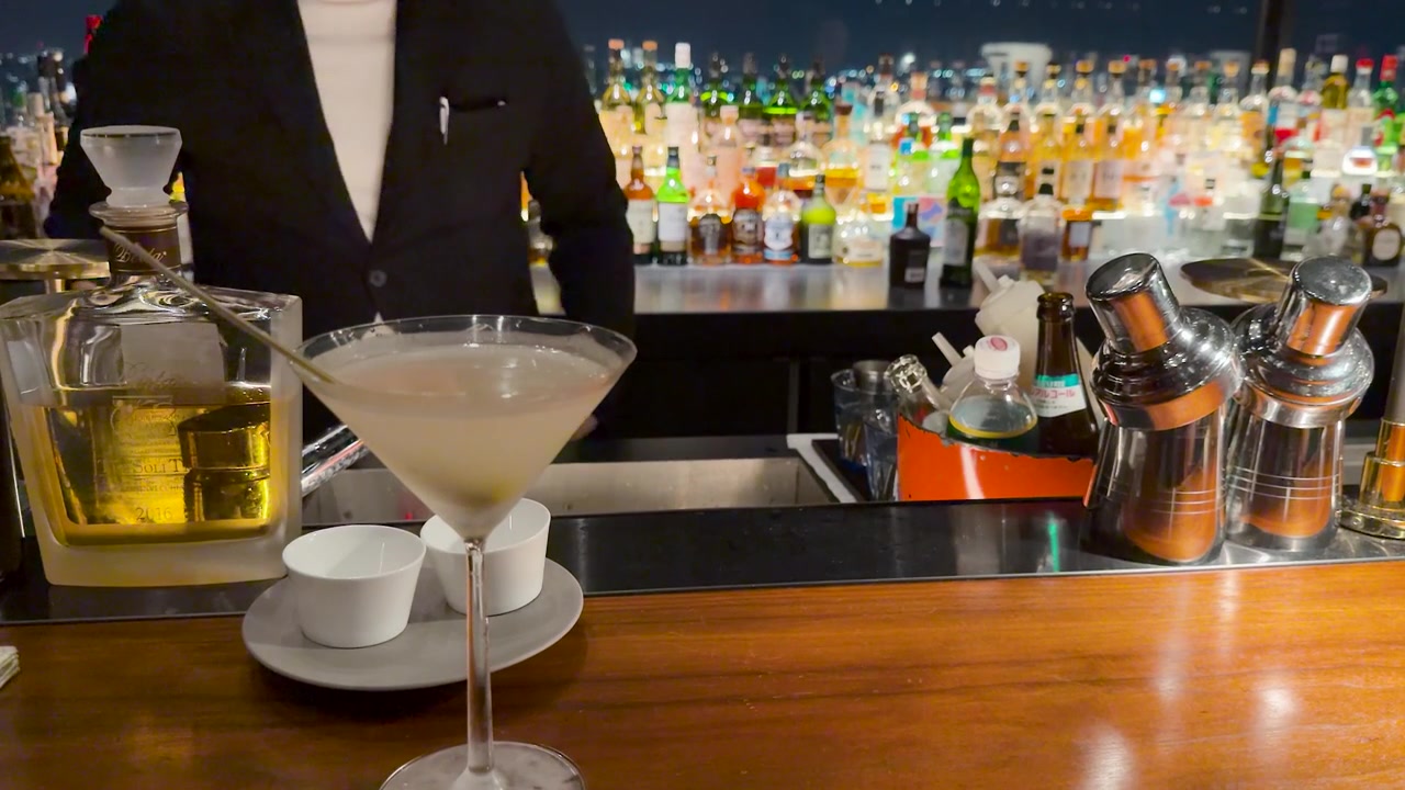 Un barman professionista in abito nero prepara bevande dietro un bancone del bar ben fornito.
