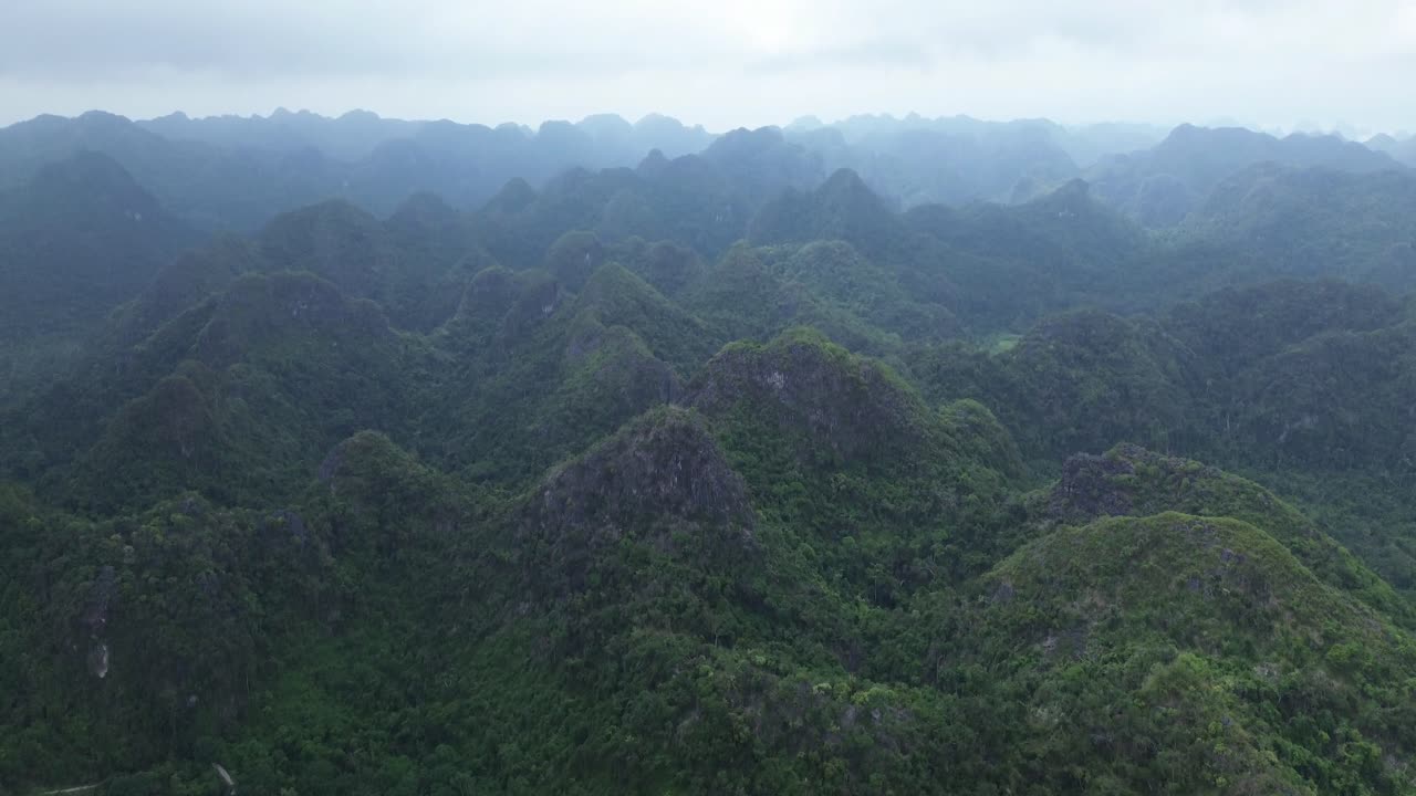 Camera angle elevates while drone rises above limestone ridges and forest of Cat Ba Island