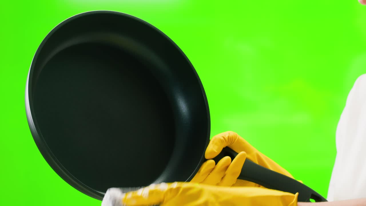 Hand in gelbem Handschuh wäscht Bratpfanne auf grünem Bildschirm