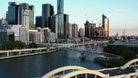 Aerial-view-of-downtown-cityscape-and-William-Jolly-bridge-spanning-across-the-river-at-sunset,-luxury-apartment-properties,-riverside-corporate-buildings-at-central-business-district,-Brisbane-city