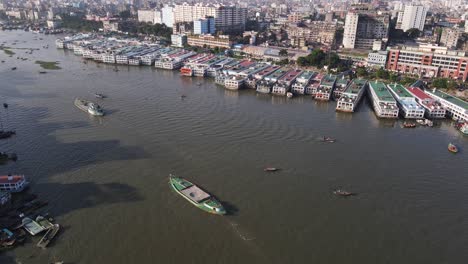 aerial: dockyard at buriganga river bank with city landscape in dhaka, bangladesh - drone tilt up shot