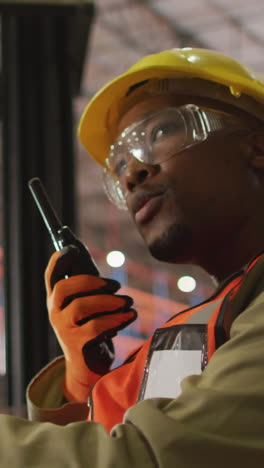 african american male worker wearing safety suit with helmet talking in warehouse