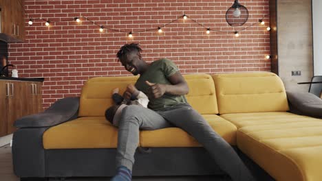 African-father-playing-with-little-adorable-child-son-having-fun-on-sofa