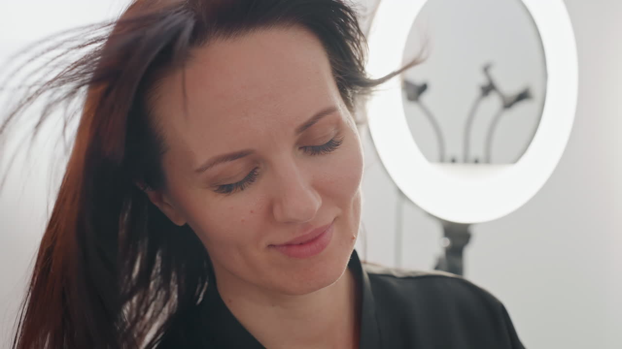 Ritratto in studio di una donna caucasica, consulenza in un salone, leggera inclinazione della testa, sorriso delicato, sfondo con anello luminoso, leggero movimento dei capelli, stilista che prepara la cliente, atmosfera moderna e minimalista del salone