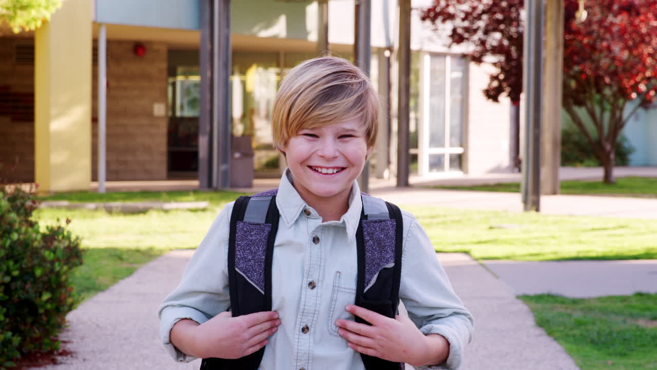 escolar blanco caminando hacia la cámara fuera del edificio de la escuela