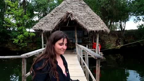 mujer joven sonriendo tímidamente frente a una choza en una laguna tropical en méxico