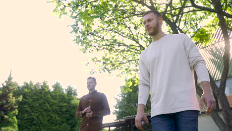 bottom view of caucasian young man throwing a petanque ball in the park on a sunny day while his male friend waits his turn