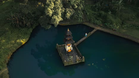 Woman-visiting-ancient-holy-temple-in-blue-pond-in-tropical-Bali,-aerial