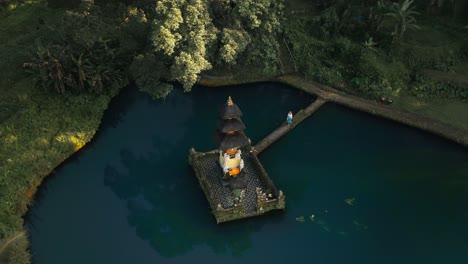 woman visiting ancient holy temple in blue pond in tropical bali, aerial