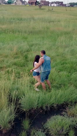 wonderful upper view brunette girl in white t-shirt and denim shorts jumps into man arms on green meadow