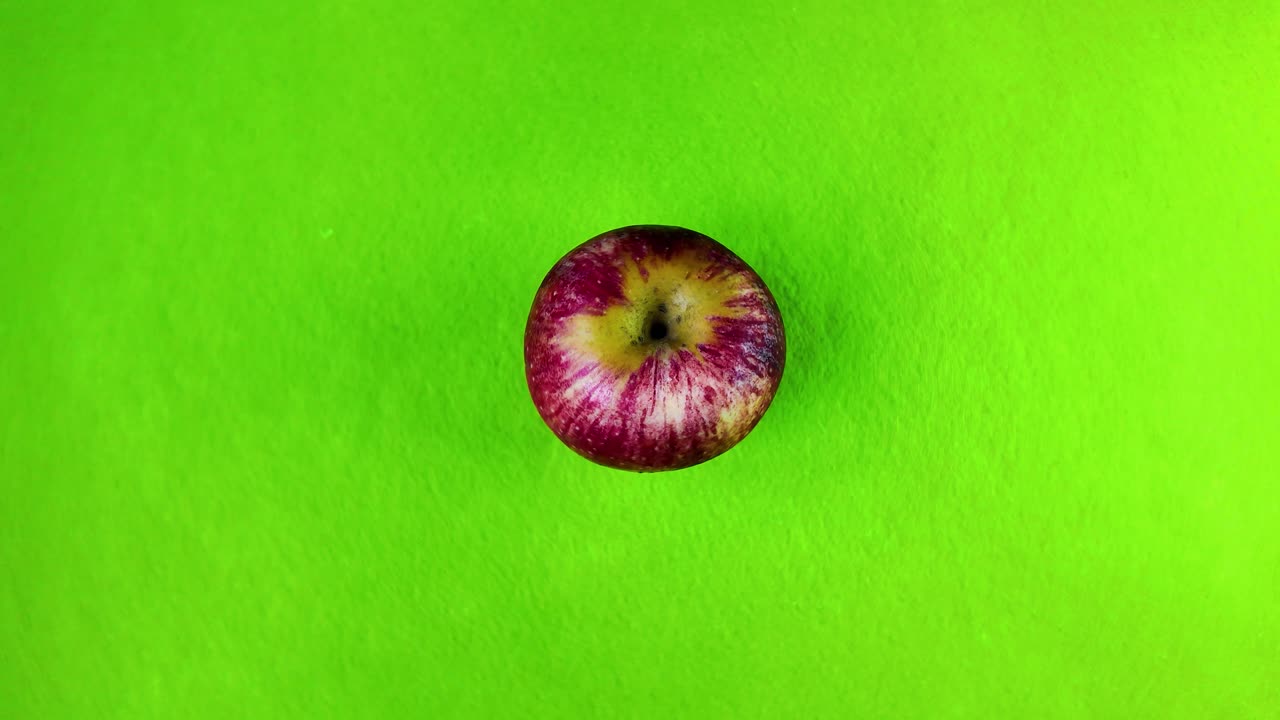 Single red apple rotating on a bright green background