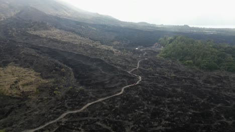 lone vehicle drives on dirt road across volcanic lava field in bali