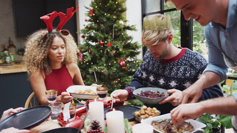 group of friends sitting around dining table at home as vegetarian christmas dinner is served