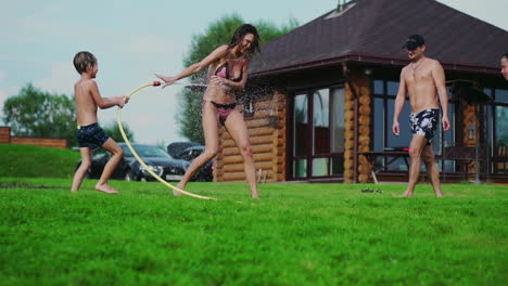 family in the backyard of a country house in the summer relax playing with water and hosing