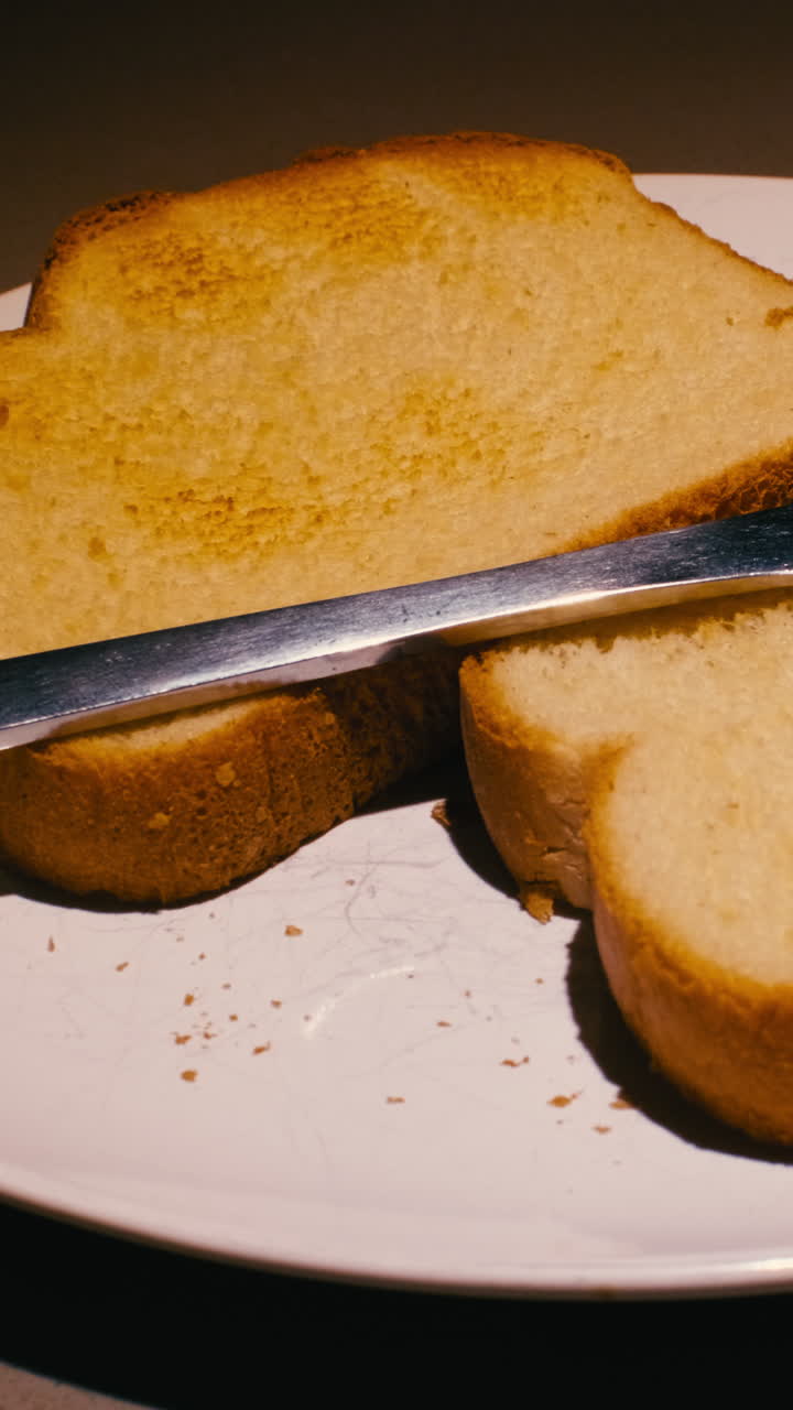 Macro vertical shot of freshly toasted bread slices on a white ceramic plate with a steel knife during breakfast time