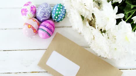 multicolored easter eggs, bunch of flower and envelope on wooden surface