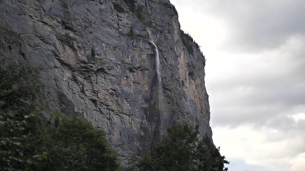 Water falling down between the rocks and green trees from a high waterfall in Lauterbrunnen in Switserland on a cloudy day. Wide shot