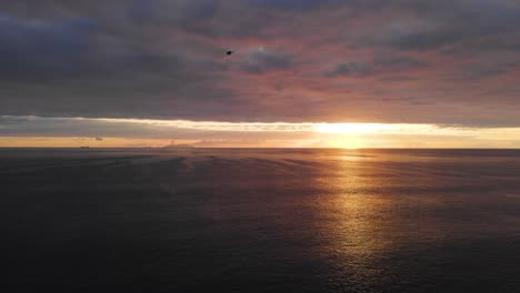 Pájaro-Volando-Sobre-Un-Océano-En-Calma,-Contra-Un-Amanecer-Nublado