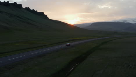 Birds-eye-view-car-peacefully-driving-on-ring-road,-the-most-important-highway-in-Iceland.-Aerial-view-car-driving-along-empty-country-road-at-golden-sunset