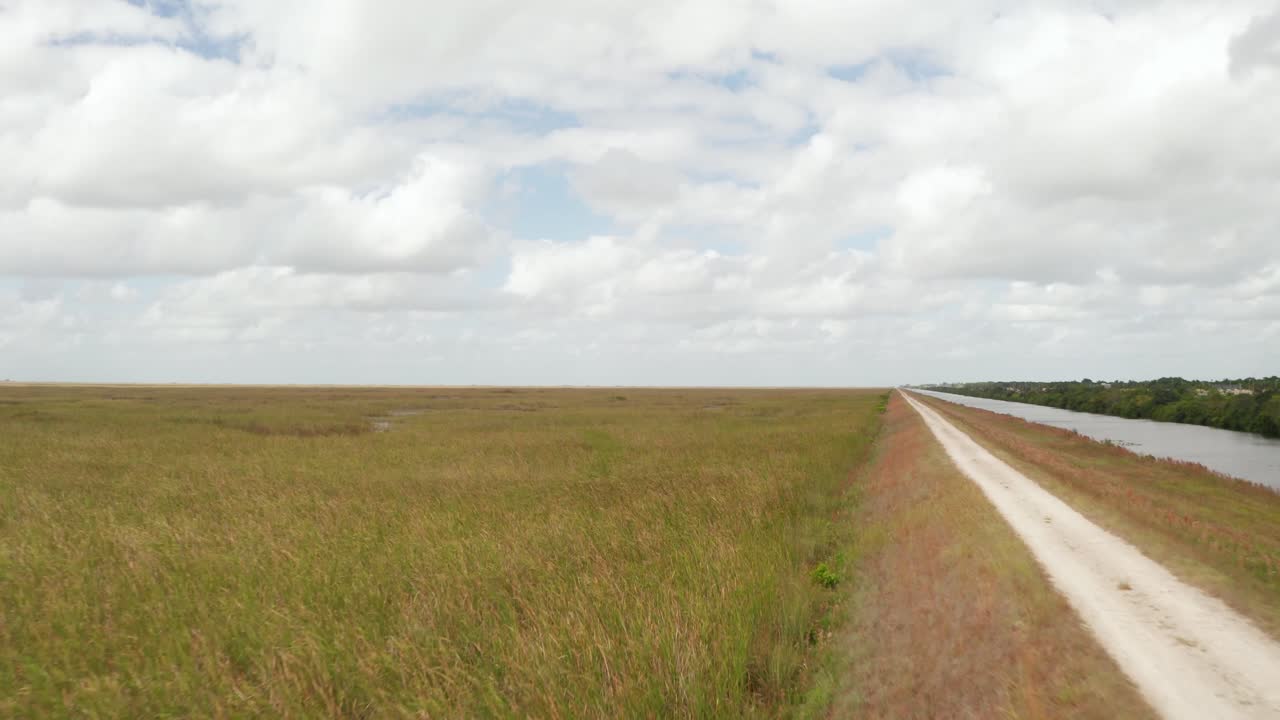 tomada de avión no tripulado de la hierba de sierra en los everglades de florida, cerca del área de sierra al lado del dique. moviéndose hacia adelante más allá del camino de tierra en la cubierta de nubes