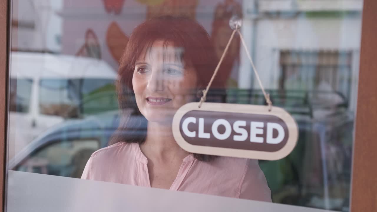 Happy woman changing closed to open sign on window smiling looking outside waiting for clients. Start-up concept.
