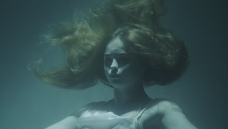 closeup of a beautiful girl with red hair in a white dress froze under water