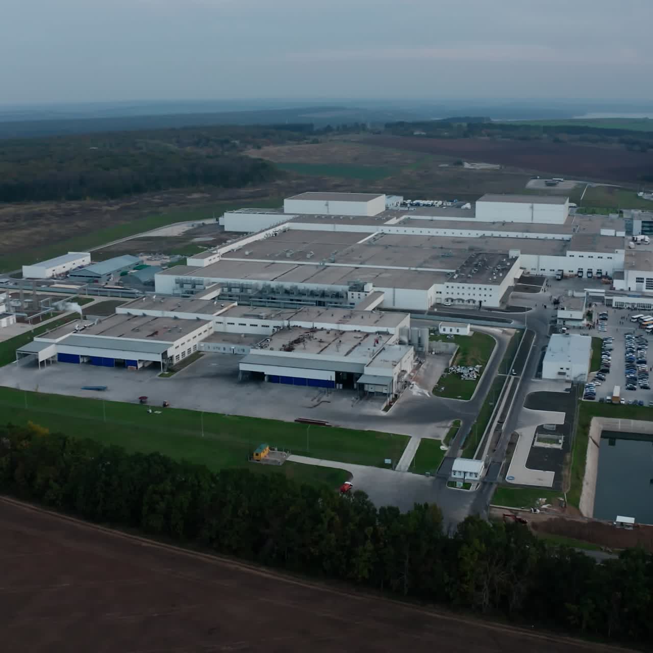 Industrial zone in the countryside. Large territory of a modern plant with car parking among environment. New factory on field. Aerial view.