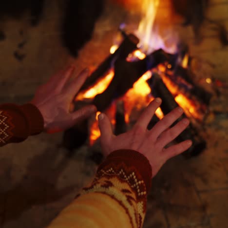 man warming hands by the fire indoors. cozy fireplace with burning wooden logs and flame warming male's hands . close-up.