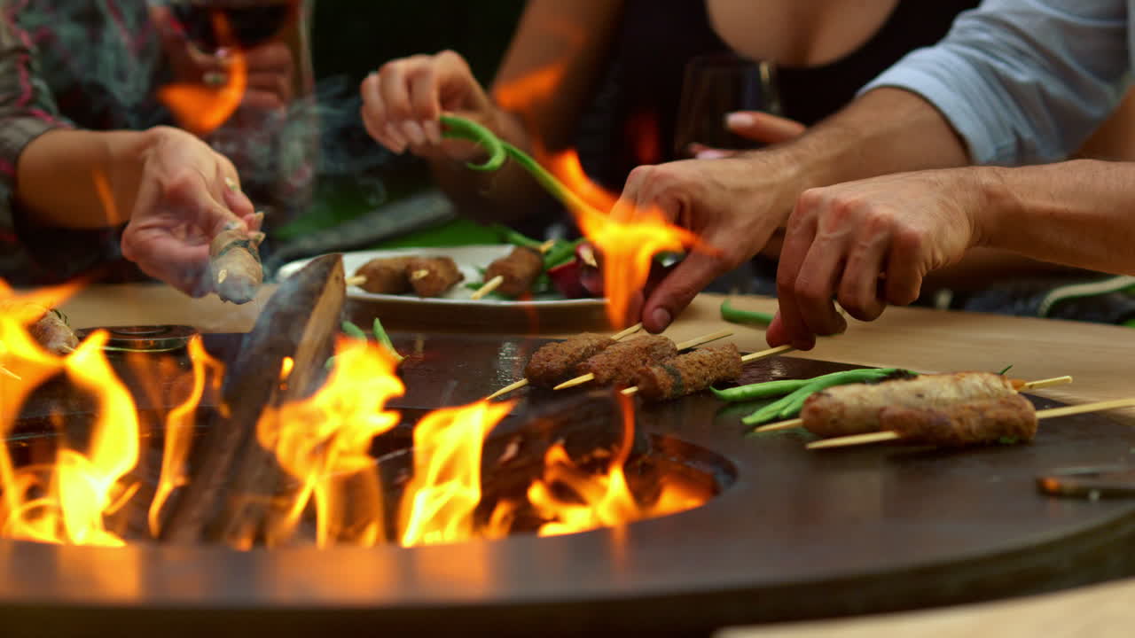 Persone sconosciute grigliano carne e verdure all'aperto. Amici che cucinano fuori.