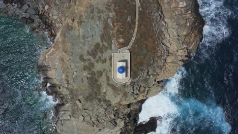 an aerial birds eye view of a small church in a greek island, between the cliffs and the sea